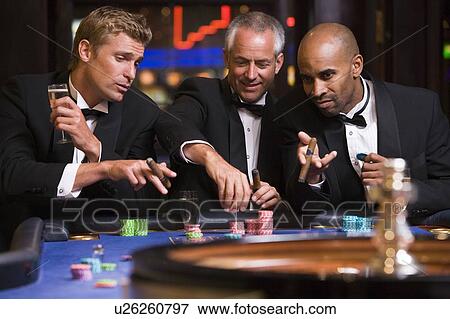 Three men in casino playing roulette and smiling (selective focus) View Large Photo Image Stock Photo - Three men in casino playing roulette and smiling (selective focus). Fotosearch