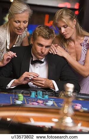 Stock Image - Three people in casino playing roulette smiling (selective focus). Fotosearch