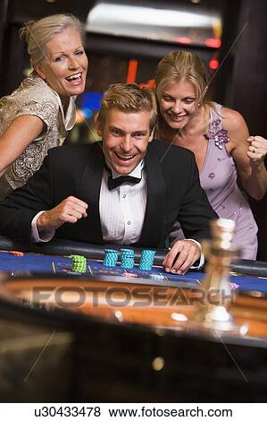 Stock Photo - Three people in casino playing roulette smiling (selective focus). Fotosearch