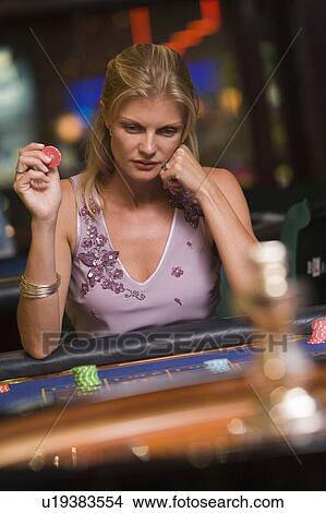 Picture - Woman in casino playing roulette and holding chip (selective focus). Fotosearch