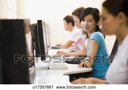 Stock Image - Four people sitting in computer room smiling. Fotosearch