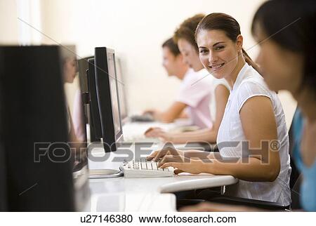 Stock Image - Four people sitting in computer room typing and smiling. Fotosearch