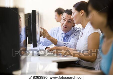 Stock Image - Man assisting woman in computer room. Fotosearch