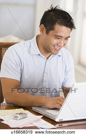 Man in dining room using laptop and smiling View Large Photo Image Stock Photo - Man in dining room using laptop and smiling. Fotosearch
