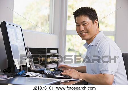 Stock Image - Man in home office using computer and smiling. Fotosearch