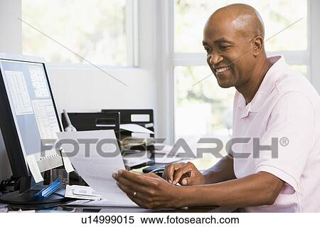 Stock Photography - Man in home office using computer and smiling. Fotosearch