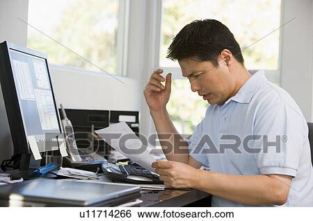 Stock Photograph - Man in home office with computer and paperwork frustrated. Fotosearch
