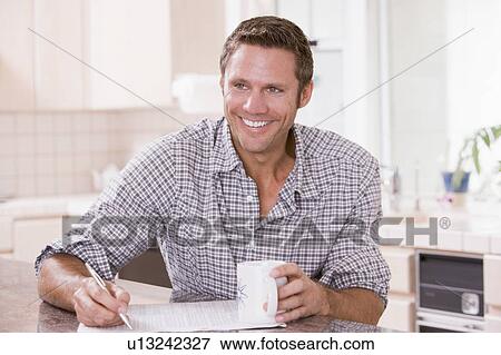 Man in kitchen reading newspaper and smiling View Large Photo Image Stock Photo - Man in kitchen reading newspaper and smiling. Fotosearch