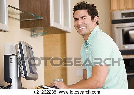 Man in kitchen using computer and smiling View Large Photo Image Stock Photo - Man in kitchen using computer and smiling. Fotosearch