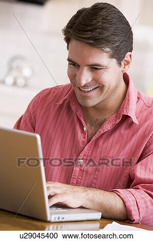 Man in kitchen using laptop smiling View Large Photo Image Stock Image - Man in kitchen using laptop smiling. Fotosearch