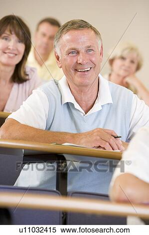 Stock Photography - Man sitting in adult classroom laughing with students in background (selective focus). Fotosearch