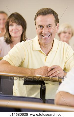 Man sitting in adult classroom with students in background (selective focus) View Large Photo Image Stock Photography - Man sitting in adult classroom with students in background (selective focus). Fotosearch