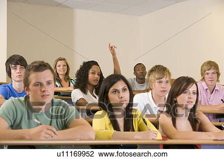 Stock Image - Students in class paying attention and taking notes with one volunteering (selective focus). Fotosearch