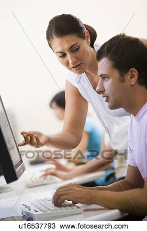 Stock Image - Woman assisting man in computer room. Fotosearch