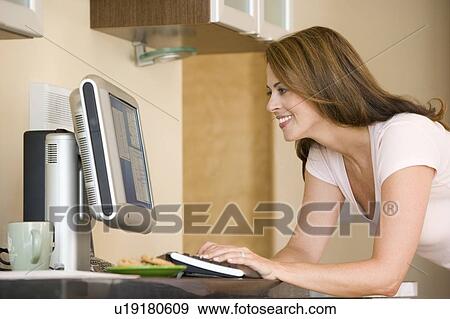 Stock Photo - Woman in kitchen with computer smiling. Fotosearch