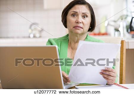 Woman in kitchen with laptop and paperwork looking worried View Large Photo Image Stock Image - Woman in kitchen with laptop and paperwork looking worried. Fotosearch