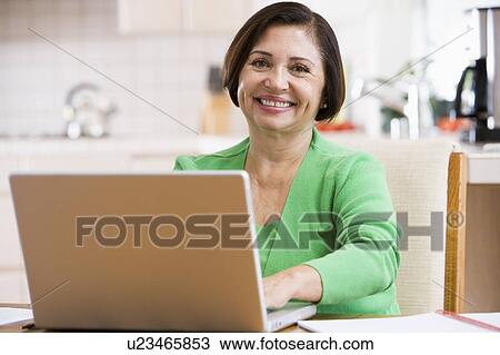 Stock Image - Woman in kitchen with laptop smiling. Fotosearch
