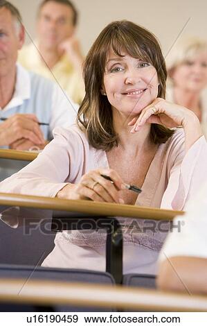 Stock Photo - Woman sitting in adult classroom with students in background (selective focus). Fotosearch