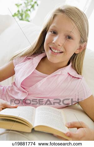 Picture - Young Girl Sitting On A Sofa Reading A Book. Fotosearch