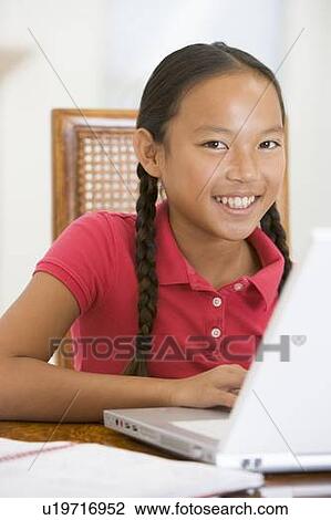 Stock Image - Young girl with laptop in dining room smiling. Fotosearch