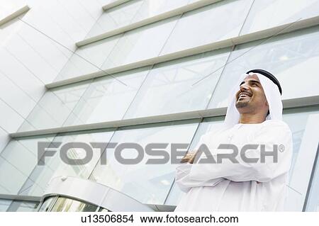 Picture - Businessman standing outdoors by building smiling. Fotosearch