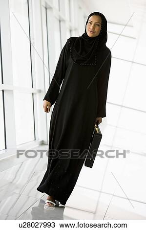 Stock Image - Businesswoman walking in a corridor with a briefcase and smiling (high key/selective focus). Fotosearch