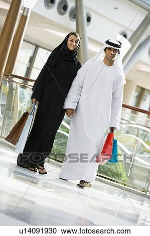 Stock Image - Couple walking in mall holding hands and smiling (selective focus). Fotosearch