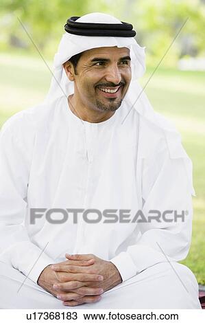 Stock Image - Man sitting outdoors in park smiling (selective focus). Fotosearch