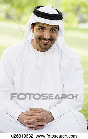 Stock Image - Man sitting outdoors in park smiling (selective focus). Fotosearch