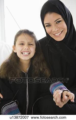 Stock Photo - Mother and young girl in living room holding hands and smiling (high key/selective focus). Fotosearch