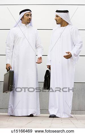 Two businessmen standing outdoors with briefcases talking View Large Photo Image Stock Photo - Two businessmen standing outdoors with briefcases talking. Fotosearch