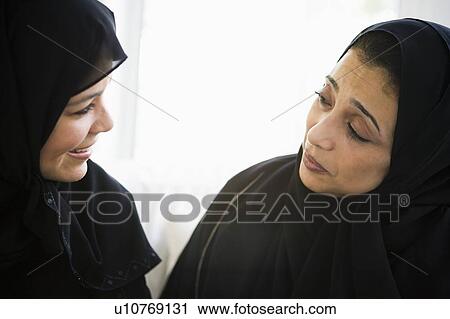 Stock Image - Two women sitting indoors talking and smiling (high key). Fotosearch