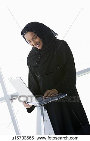 Stock Photography - Woman indoors standing with laptop and smiling (high key/selective focus) . Fotosearch