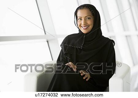 Stock Image - Woman sitting indoors smiling (high key/selective focus). Fotosearch