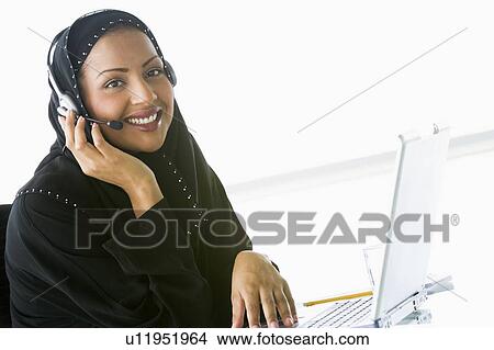 Woman wearing headset with laptop smiling (high key/selective focus) View Large Photo Image Picture - Woman wearing headset with laptop smiling (high key/selective focus). Fotosearch