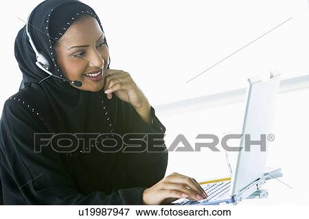 Stock Photo - Woman wearing headset with laptop smiling (high key/selective focus). Fotosearch