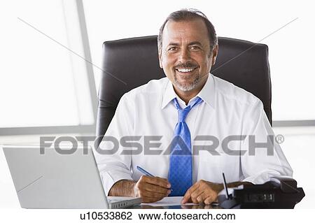 Stock Image - Businessman in office with laptop smiling (high key/selective focus). Fotosearch