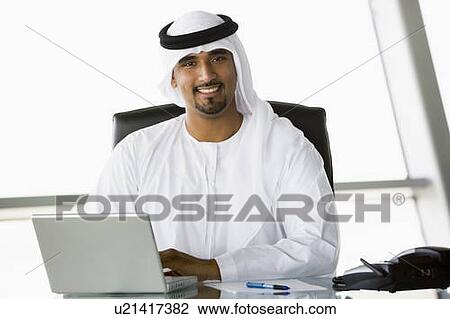 Stock Image - Businessman in office with laptop smiling (high key/selective focus). Fotosearch