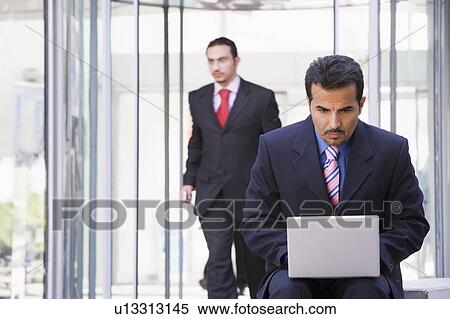 Businessman outdoors in front of building using laptop with businessman in background (high key/selective focus) View Large Photo Image Stock Photography - Businessman outdoors in front of building using laptop with businessman in background (high key/selective focus). Fotosearch