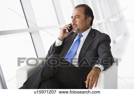 Businessman sitting indoors on cellular phone (high key/selective focus) View Large Photo Image Stock Photo - Businessman sitting indoors on cellular phone (high key/selective focus). Fotosearch