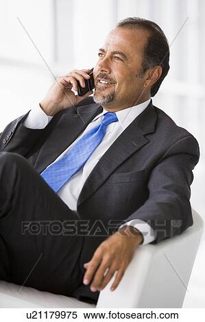 Stock Photography - Businessman sitting indoors on cellular phone smiling (high key/selective focus). Fotosearch