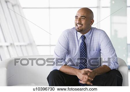 Businessman sitting indoors smiling (high key/selective focus) View Large Photo Image Stock Image - Businessman sitting indoors smiling (high key/selective focus). Fotosearch
