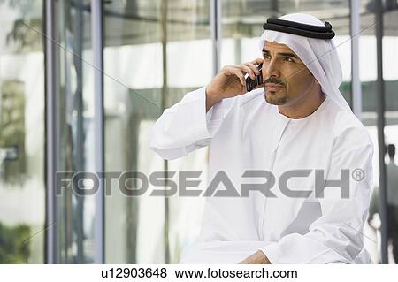 Stock Photo - Businessman sitting outdoors by building using cellular phone (selective focus). Fotosearch