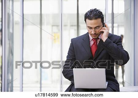 Stock Photo - Businessman sitting outdoors by building with a laptop on cellular phone (high key/selective focus). Fotosearch