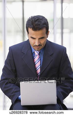 Businessman sitting outdoors by building with a laptop (high key/selective focus) View Large Photo Image Stock Photo - Businessman sitting outdoors by building with a laptop (high key/selective focus). Fotosearch