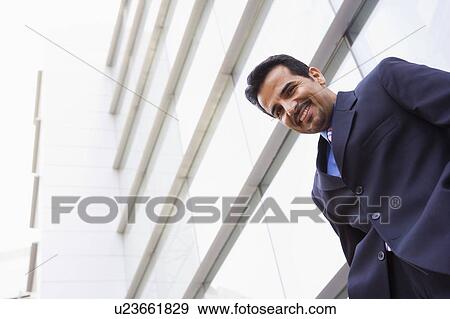 Businessman standing outdoors by building smiling (high key/selective focus) View Large Photo Image Stock Photo - Businessman standing outdoors by building smiling (high key/selective focus). Fotosearch