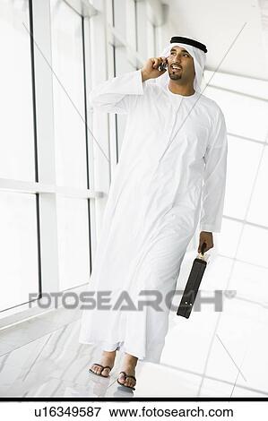 Stock Photo - Businessman walking in a corridor on a cellular phone and smiling (high key/selective focus). Fotosearch