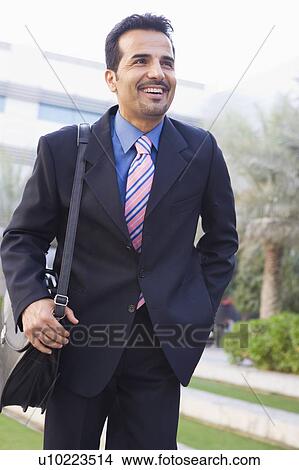 Businessman walking outdoors smiling (high key/selective focus) View Large Photo Image Picture - Businessman walking outdoors smiling (high key/selective focus). Fotosearch