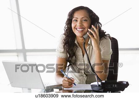 Businesswoman in office on telephone by laptop smiling (high key/selective focus) View Large Photo Image Stock Photo - Businesswoman in office on telephone by laptop smiling (high key/selective focus). Fotosearch
