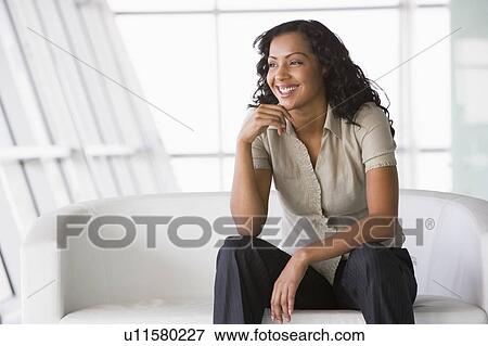 Stock Photo - Businesswoman sitting indoors smiling (high key/selective focus). Fotosearch